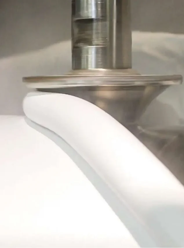 A metal tool smoothly shaping a thick band of white material over a curved white surface