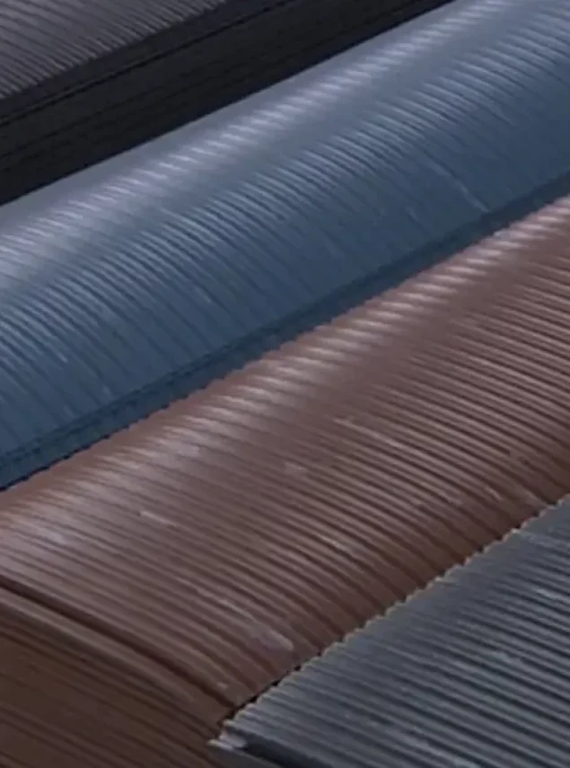 Stacked stacks of curved, corrugated metal roofing sheets in dark grey, blue, and brown