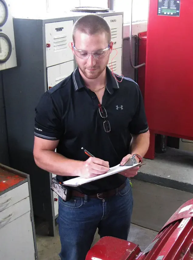 Technician wearing safety glasses and writing on a clipboard in an industrial facility