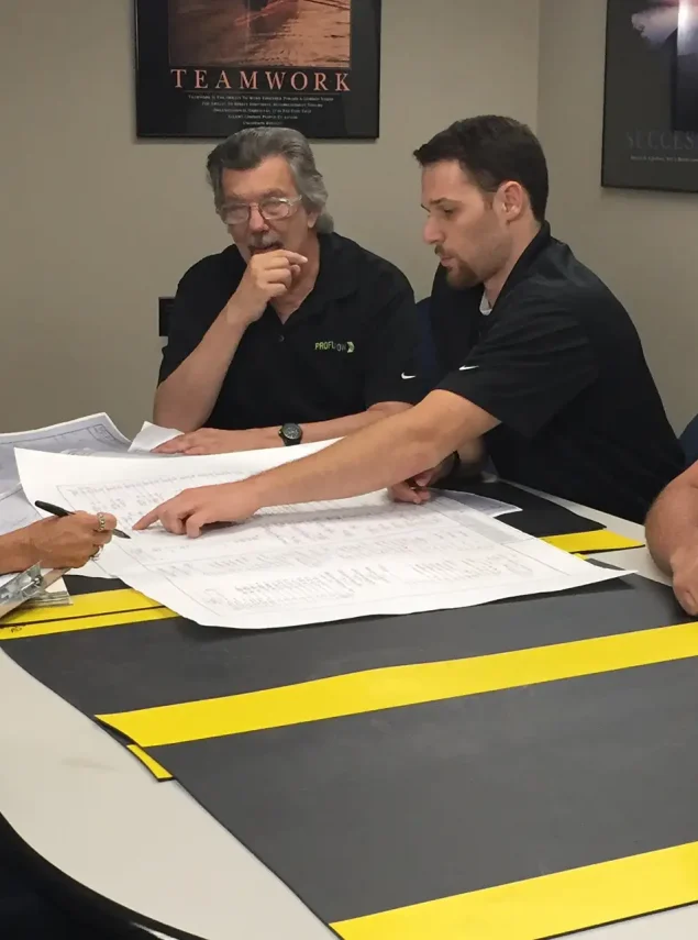 Five people gathered around a conference table reviewing architectural blueprints